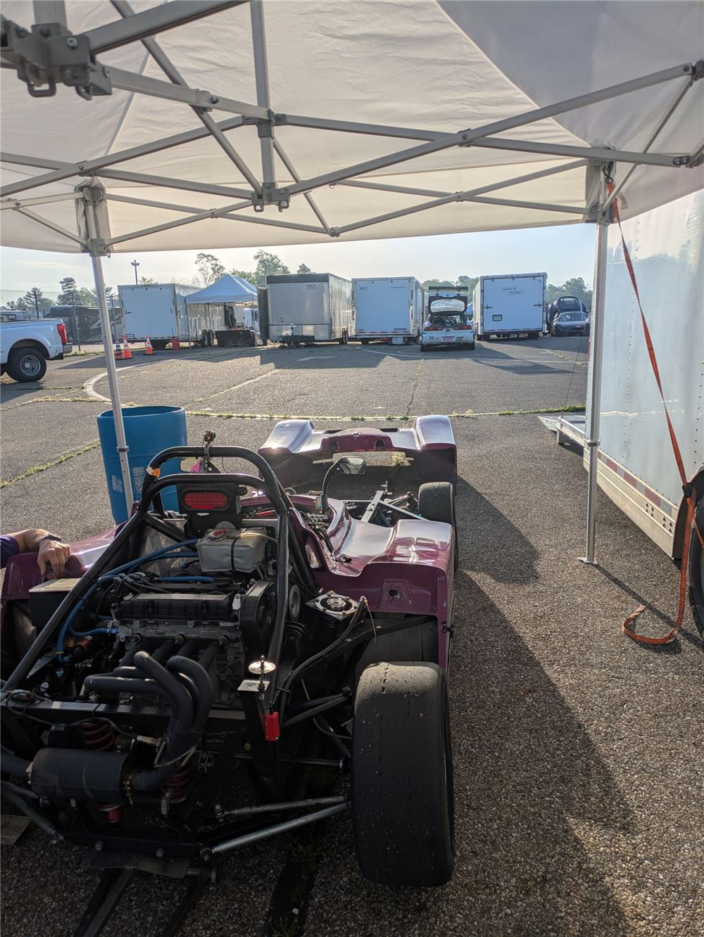 Spec Racer Ford under a canopy in the Mid-Ohio paddock with trailers behind it