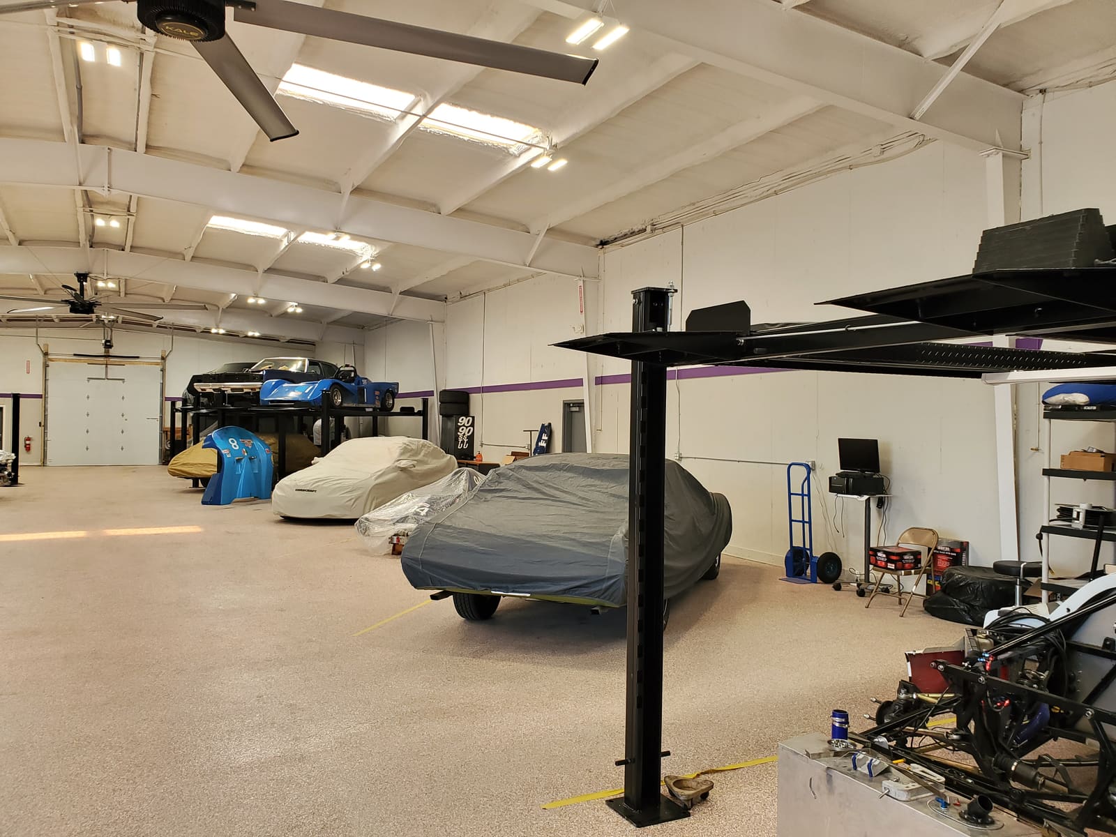 Race cars stored on a stacking lift above covered street cars at B2 Motorsports