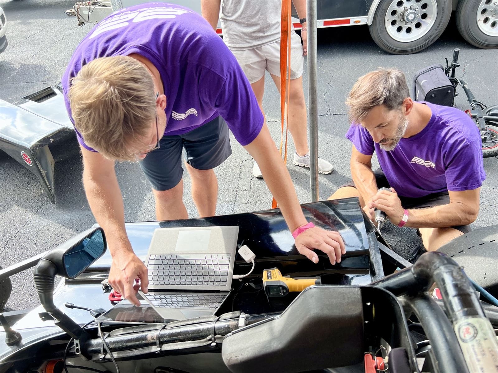 B2 Motorsports crew in purple reviewing driver data on a laptop in the paddock